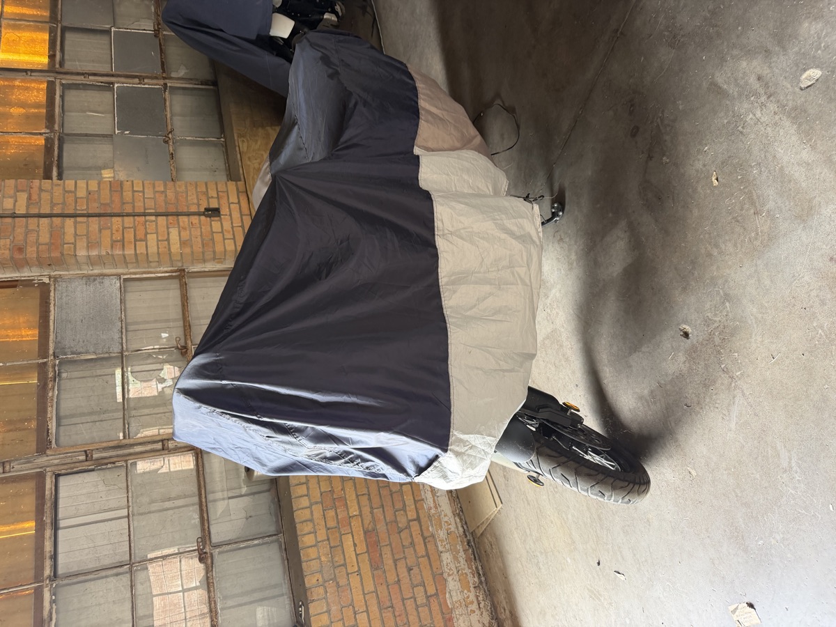 Motorcycle under a fitted cover along the brick wall